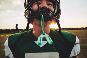 Closeup of a young American football player with his mouthguard hanging from his helmet during a team practice session